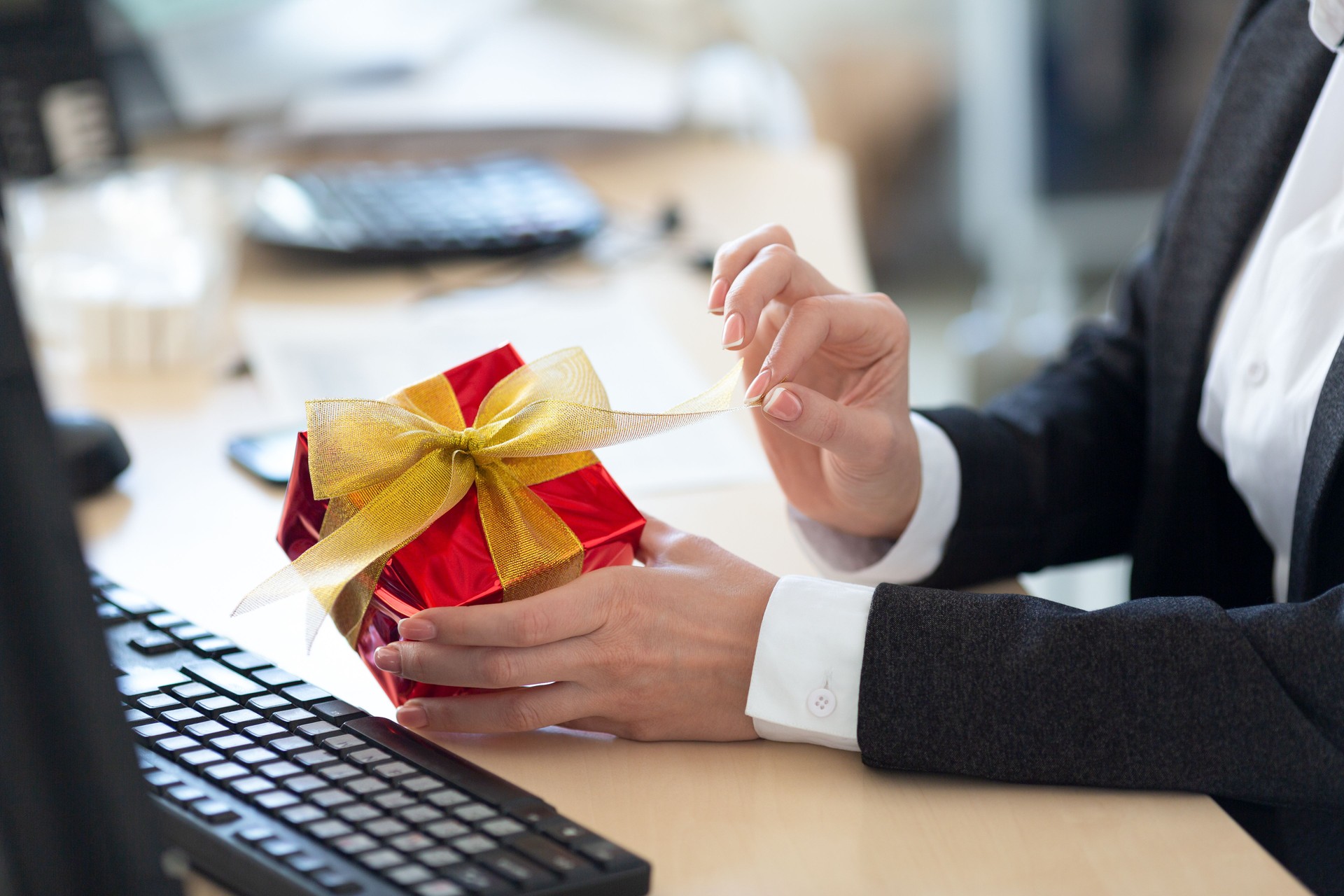 Greetings with Valentines Day at work. Female hands open a red giftbox on the desk in office, close up, selective focus.